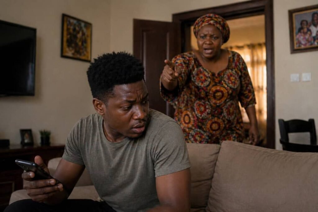 A young Black man looks tense on a couch as an older woman calls him sternly from behind in a Nigerian home.